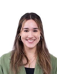 Studio headshot of a smiling woman with long brown hair, wearing hoop earrings and a green blazer on a white background.