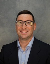Professional headshot of a smiling man wearing glasses and a blazer.