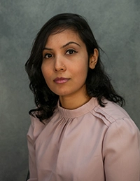 Professional headshot of a smiling woman with long dark hair, wearing a light-colored blouse.
