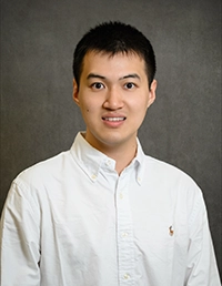 Headshot of a young man in a white collared shirt smiling at the camera.