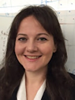 Smiling woman with long dark hair in front of a whiteboard.