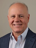 Professional headshot of a smiling man with a bald head and light complexion, wearing a blue checkered blazer over a white shirt.