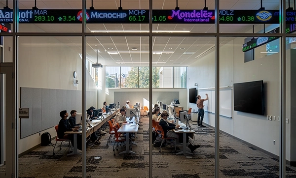A classroom setting with students engaged in a learning environment, featuring stock ticker displays at the top.