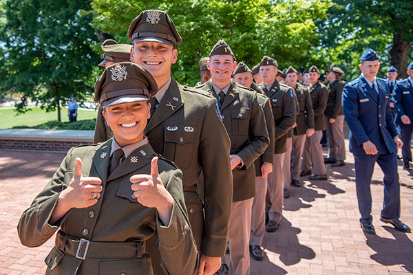 Two male and one female cadet posing in front of state and US flags for commissioning ceremony.
