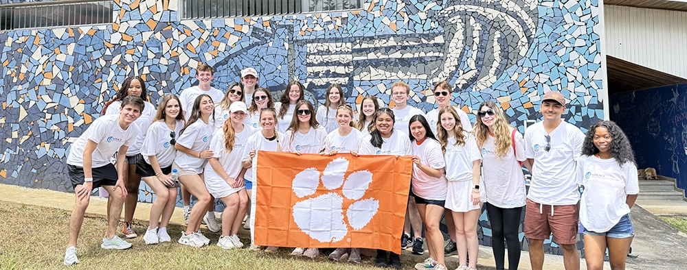 Group of students posing with a Clemson University flag in front of a colorful mural.