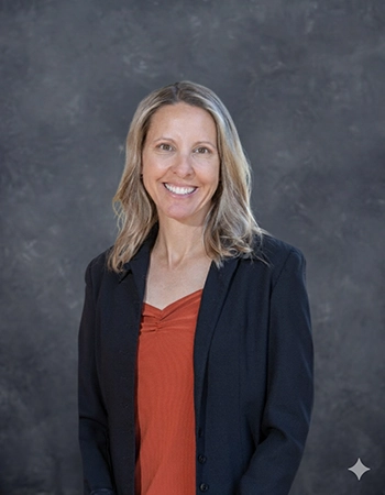 Professional headshot of a woman smiling, wearing a black blazer over an orange top, set against a textured gray background.