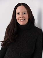 Portrait of a smiling woman with long dark hair wearing a black turtleneck against a light background.