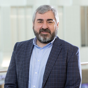 Professional portrait of a man with a beard, wearing a blue blazer over a light blue shirt.