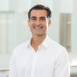 Smiling professional man wearing a white shirt, standing in a bright, modern environment.