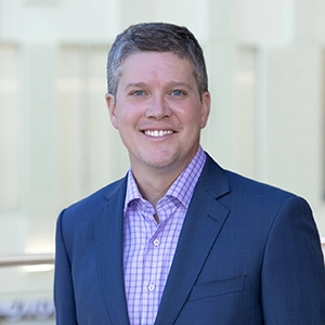 Professional portrait of a smiling man in a suit against a light background.