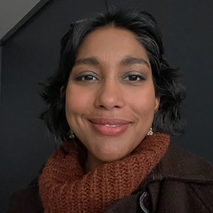 Headshot of a smiling woman with dark hair, wearing a cozy brown sweater and earrings.