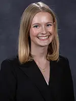 Professional headshot of a young woman with shoulder-length blonde hair, smiling and wearing a black blazer.