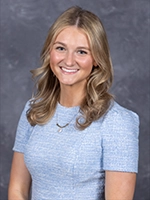 Professional headshot of a woman with blonde hair, wearing a light blue dress.