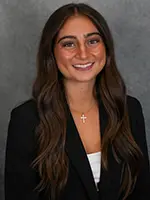 Professional headshot of a young woman with long hair, wearing a black blazer and a white top, smiling at the camera.