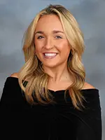 A portrait of a woman with long blonde hair smiling, wearing an off-the-shoulder black top.