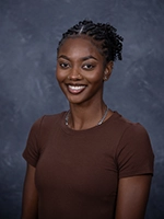 Professional headshot of a woman with braided hair, smiling against a gray background.
