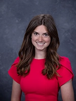 A professional headshot of a woman with long brown hair wearing a vibrant red dress.