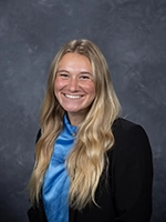 Headshot of a smiling woman with long blonde hair, wearing a black blazer and blue blouse.