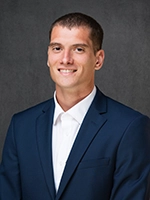 Studio headshot of a smiling man wearing a navy suit jacket and white dress shirt against a dark gray background.