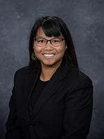 Professional portrait of a smiling woman wearing glasses and a black blazer.