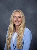 Professional headshot of a young woman with long blonde hair, wearing a light blue blazer and smiling.