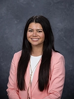 Professional headshot of a woman with long dark hair, wearing a pink blazer and smiling.