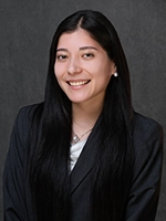 Studio headshot of a smiling woman with long dark hair wearing a dark blazer against a gray background.