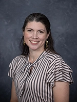 Professional headshot of a woman with long dark hair wearing a striped blouse and earrings.
