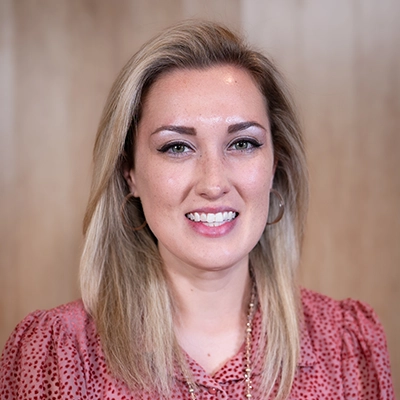 Portrait of a woman with long light hair, wearing a pink top and smiling warmly.