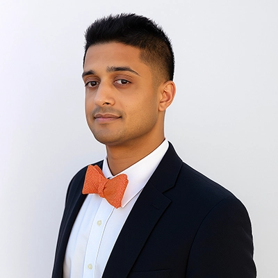 A professional portrait of a man in a suit with an orange bow tie, displaying a confident expression.