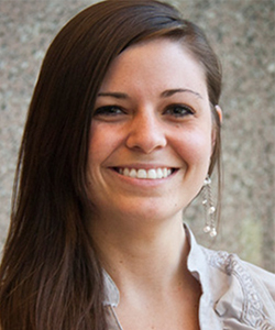 Portrait of a smiling woman with long brown hair and wearing a light gray blouse.