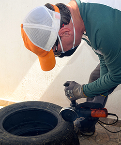 A person wearing a cap and protective gear is using a power tool to work on a tire.