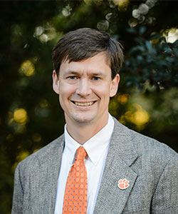 Portrait of a man wearing a grey suit jacket and orange tie, smiling outdoors.