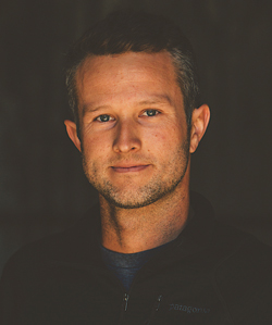 Portrait of a man with short hair and a slight smile, wearing a black jacket.