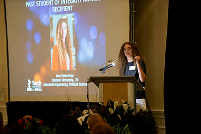 Female standing at podium speaking to audience.