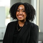 Portrait of a smiling person in a black blazer in an office setting.