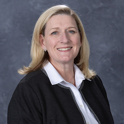 Professional headshot of a smiling woman with shoulder-length blonde hair, wearing a black blazer over a white shirt.
