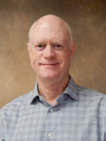 Professional headshot of a smiling man with short hair, wearing a checked shirt.