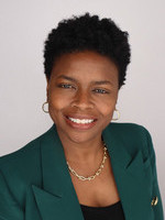Professional headshot of a woman with short curly hair, wearing a green blazer and gold earrings, smiling confidently.