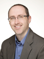 Professional headshot of a smiling man wearing glasses and a blazer.