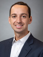 Professional headshot of a young man in a suit, smiling at the camera.