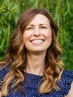 Smiling woman with long, wavy hair wearing a blue polka dot dress against a green background.