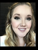 A smiling woman with wavy blonde hair and dramatic makeup showcasing a flawless complexion.