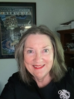 A smiling woman with shoulder-length hair, wearing a black shirt, poses for a selfie in an office setting.