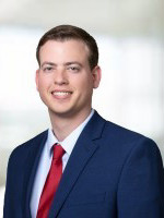 Professional headshot of a smiling man in a blue suit and red tie.