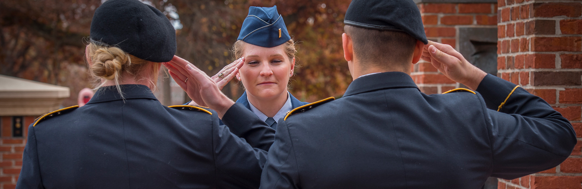 Female cadet in dress uniform saluting male and female officer.