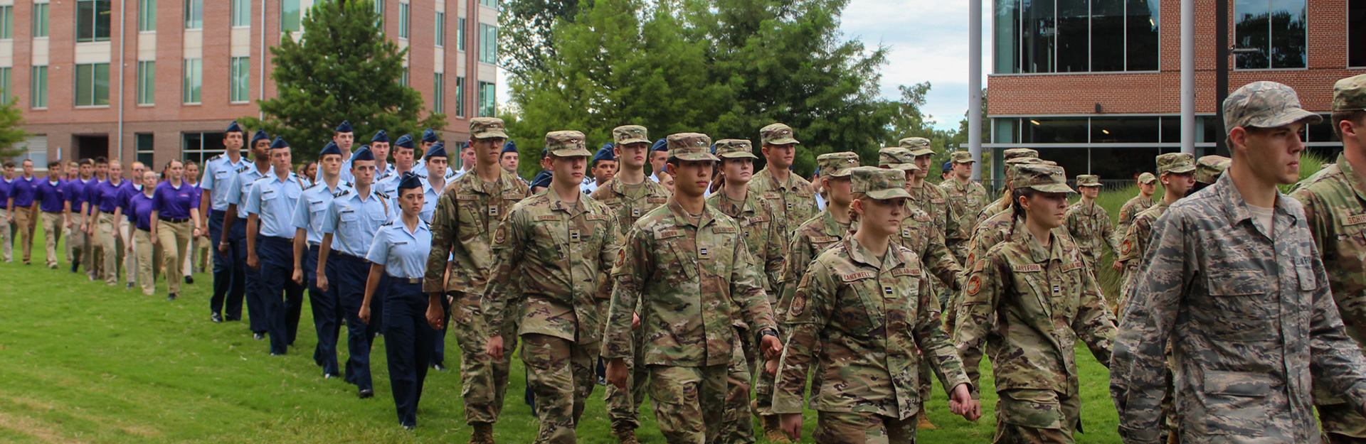 Cadets in dress uniform marching along sidewalk.