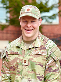 U.S. Air Force service member in camouflage uniform, smiling outdoors.