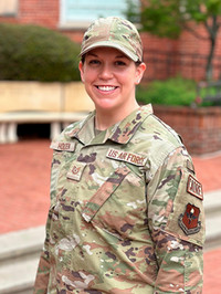 A smiling member of the U.S. Air Force in military uniform standing outside.