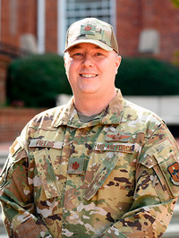 U.S. Army soldier in camouflage uniform smiling outdoors.